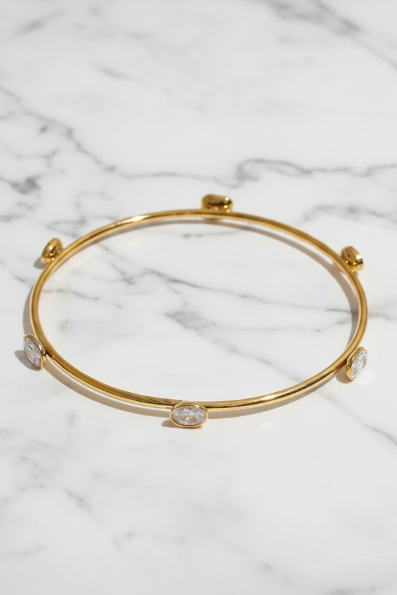 A gold-plated bangle bracelet with five clear round-cut crystals set along the band, displayed on a clean white background.